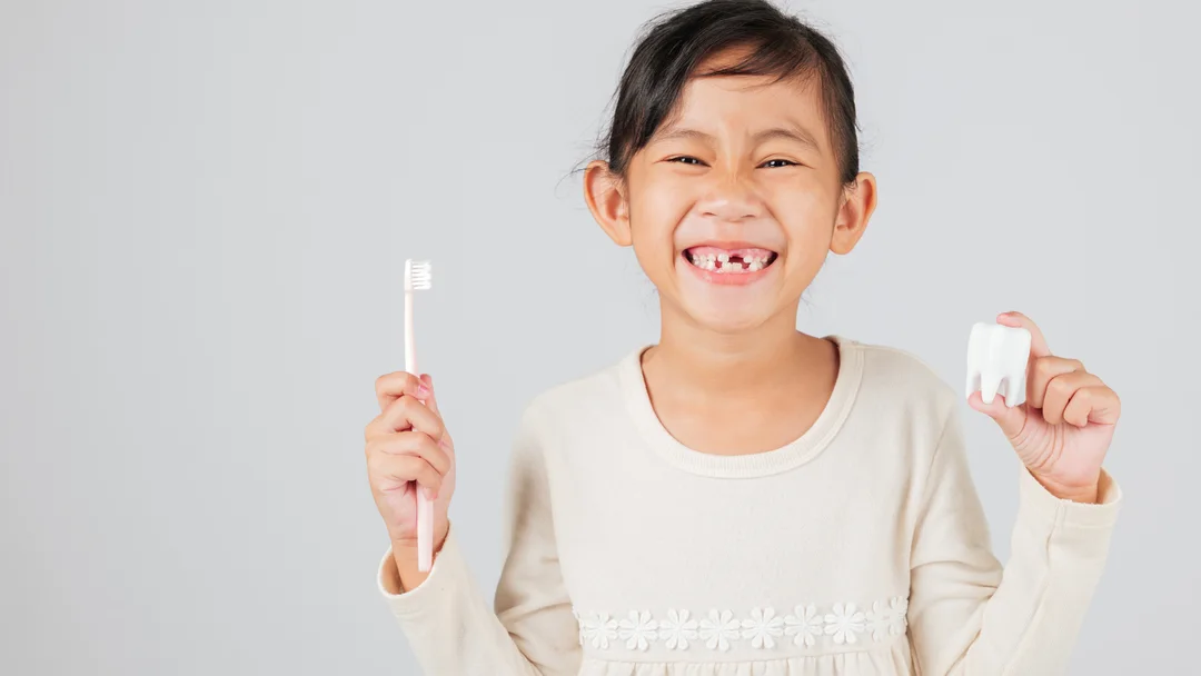 A young patient smiling at Dental Group of Mentor, holding a toothbrush and a model tooth